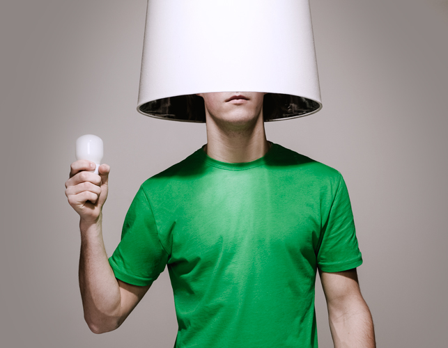 Man met groen shirt heeft een lampenkap op zijn hoofd en een lamp in zijn hand